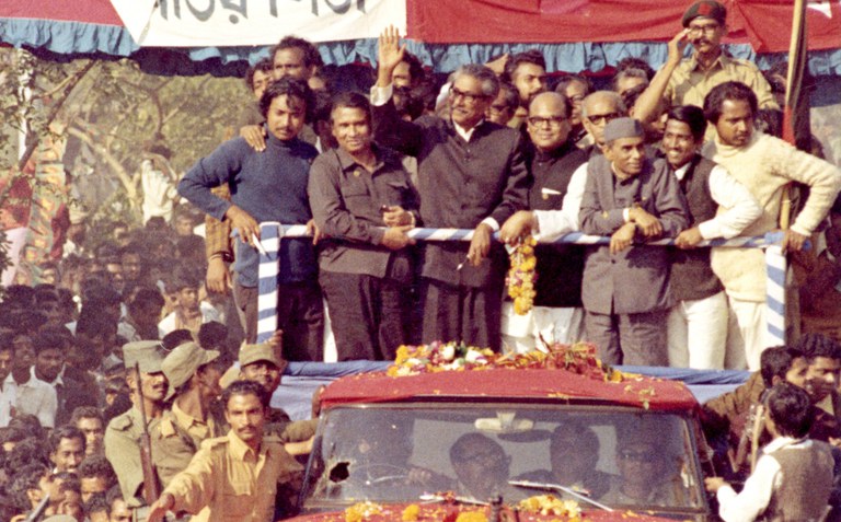 নয় মাস পাকিস্তানের জেলে কাটিয়ে স্বাধীন দেশে প্রত্যাবর্তনের পর মোটর শোভাযাত্রা থেকে জনতাকে অভিনন্দন জানাচ্ছেন বাংলাদেশের প্রতিষ্ঠাতা শেখ মুজিবুর রহমান। তাঁর বামপাশে মুজিবনগর সরকারের প্রধানমন্ত্রী তাজউদ্দীন আহমেদ। ৭৫’র আগস্ট শেখ মুজিব হত্যার পর নভেম্বরে তাজউদ্দীন আহমেদসহ চার জাতীয় নেতাকে ঢাকা কেন্দ্রীয় কারাগারে হত্যা করা হয়। ১০ জানুয়ারি ১৯৭২। [এপি]