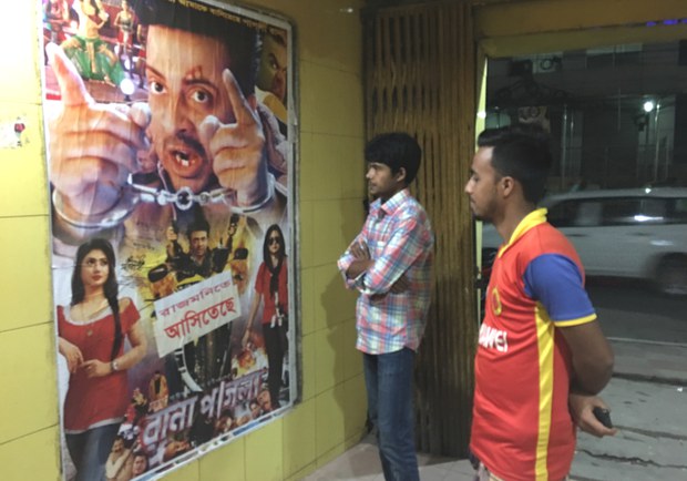 ঢাকার রাজমনি হলের সামনে সিনেমার পোস্টার দেখছেন দর্শকরা।