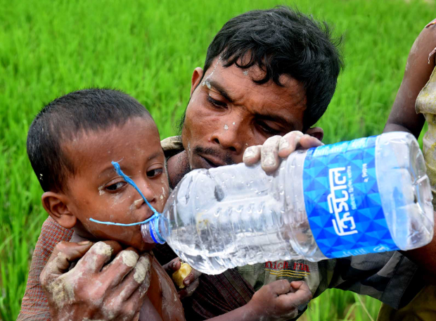 মিয়ানমার থেকে পালিয়ে এসে টেকনাফে ঢোকার পথে ক্ষুধার্ত ছেলেকে পানি পান করাচ্ছে তার বাবা। সেপ্টেম্বর ৬, ২০১৭।