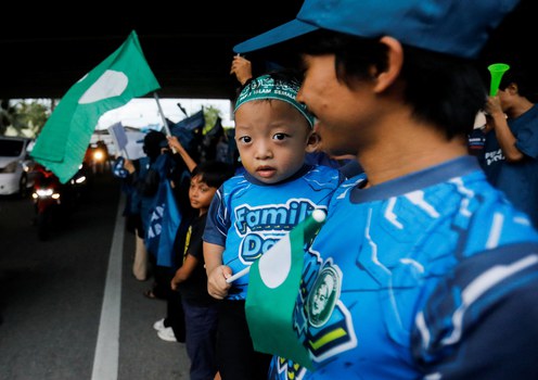 A father carries his son who holds a Malaysian Islamic Party (PAS) flag as he campaigns for PAS’ political coalition, Perikatan Nasional, in Permatang Pauh, Penang, Malaysia, Nov. 18, 2022.