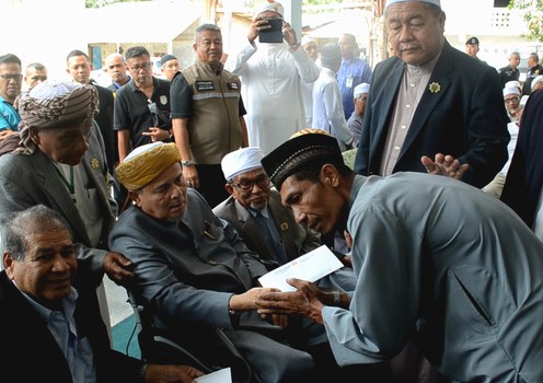 A Muslim man whose relative was shot dead by soldiers while he and other civilians foraged for wood on Dec. 16 greets Aziz Phithakumphol (left, seated), the Thai king’s adviser on Islamic affairs, as the official visits Ra-ngae district in southern Thailand’s Narathiwat province, Dec. 28, 2019. 