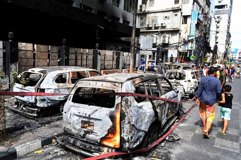 People walk past vehicles burned during unrest in Dhaka, July 19, 2024. [Munir Uz Zaman/AFP]