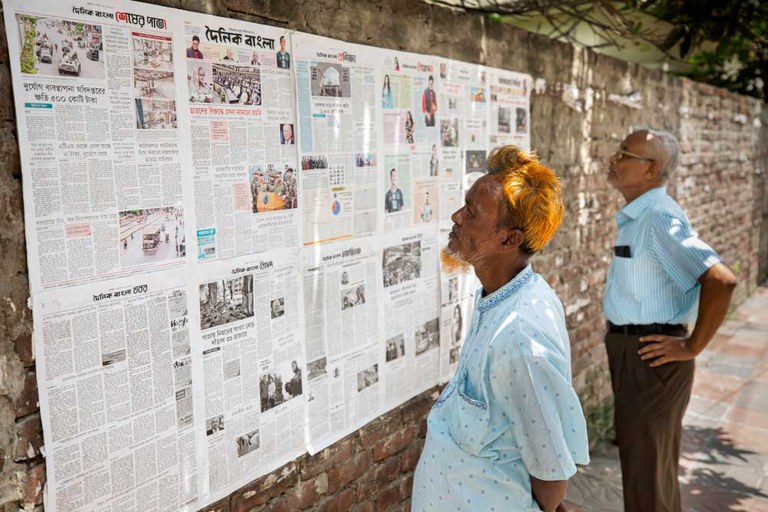 During an internet blackout in Bangladesh, two men read newspapers pasted on a wall in Dhaka, July 23, 2024. [Rajib Dhar/AP]