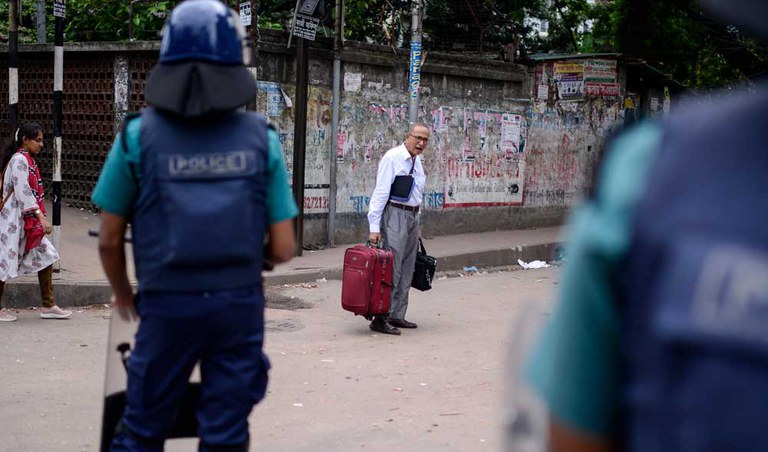 A man carrying a suitcase and other bags talks to police are he remains on a street in Dhaka during a curfew imposed after days of protest throughout Bangladesh, July 21, 2024. [Mahmud Hossain Opu/AP]