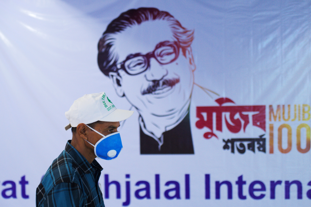 A man wearing a facemask as a preventive measure against the novel coronavirus walks past a banner with the image of Bangladesh’s founder, Sheikh Mujibur Rahman, at Hazrat Shahjalal International Airport in Dhaka, March 8, 2020. [AFP]