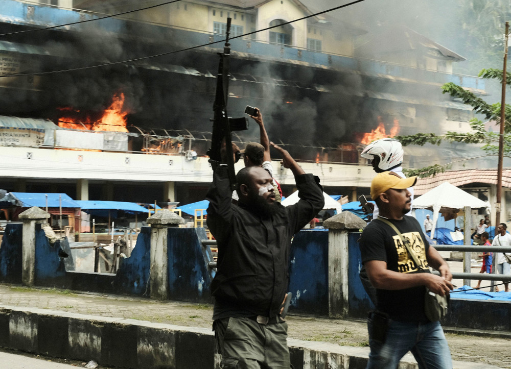A police officer raises his rifle as the local market burns during a protest in Fakfak, a regency in Indonesia’s West Papua province, Aug. 21, 2019. [AP]