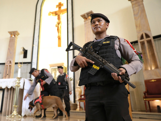 A police officer stands guard as the bomb squad lead a sniffer dog during a security sweep ahead of the Christmas holiday at The Good Shepherd Catholic Church in Surabaya, Indonesia, Monday, Dec. 23, 2019.