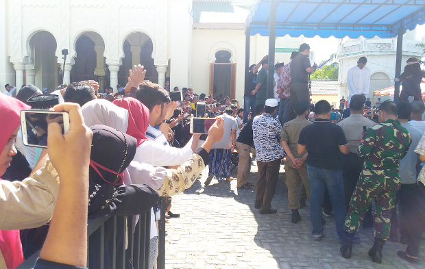 Aceh residents film a man being caned for violating Sharia law, outside a mosque in Banda Aceh, Indonesia, July 13, 2018. (Nurdin Hasan/BenarNews)