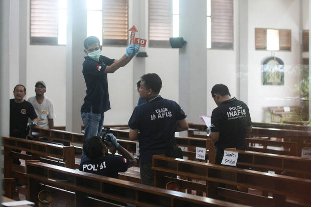 In this photograph shot through a glass window, police investigators examine the interior of St. Lidwina Church in Yogyakarta province, Indonesia, following an attack by a sword-wielding man during Sunday Mass, Feb. 11, 2018. 