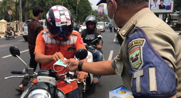 An Indonesian police officer hands out a face mask to a motorcycle rider in Padang, West Sumatra, Indonesia, Sept. 13, 2019. [Sulthan Azzam/BenarNews]