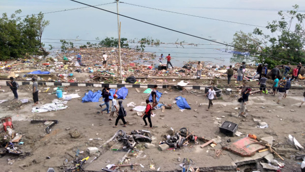 People walk past dead bodies (with blue covers) a day after two earthquakes and a tsunami hit Palu, Sulawesi, Sept. 29, 2018. [AFP]