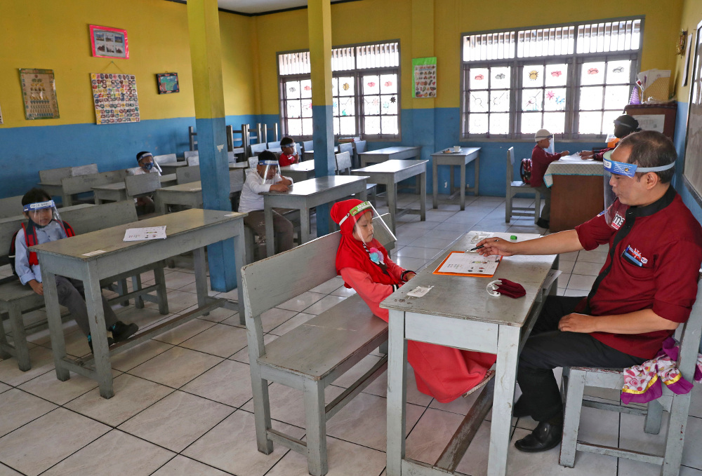 Children wearing face shields as a precaution against the new coronavirus outbreak sit spaced apart, as they wait for their turn to take an admission test at Al Hidayah Islamic Elementary School in Jakarta, July 6, 2020. [AP]