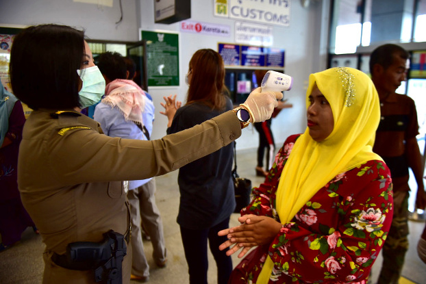 A Thai immigration officer checks the body temperature of a traveler returning from Malaysia at a border checkpoint in Narathiwat province, March 16, 2020. [Matahari Ismail/BenarNews]