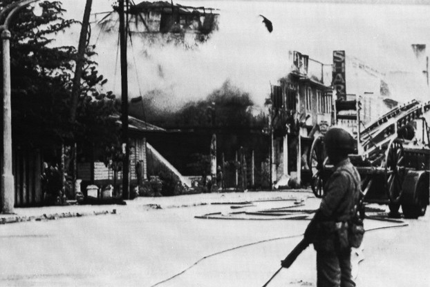 A Malaysian soldier stands guard as a fire brigade battles a blaze in some shops and homes in Kuala Lumpur, May 17, 1969. (AP)