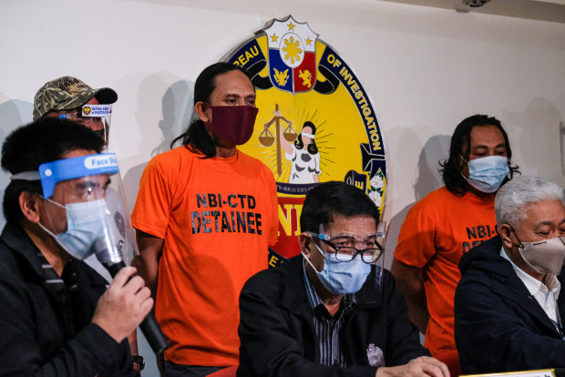 Officials with the National Bureau of Investigation announce the arrests of two suspected members of the Abu Sayyaf Group, identified as Jamar Ibi, also known as Bas, and Raden Jamil, also known as Tamiya, (standing and wearing orange shirts), at a press conference in Manila, Oct. 20, 2020. [Stringer/BenarNews]