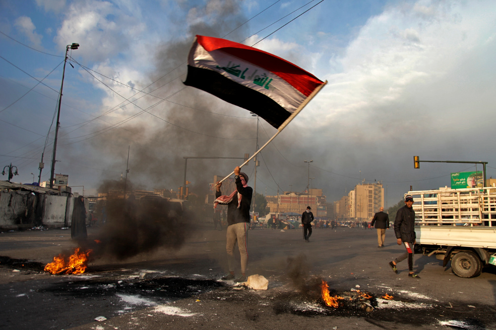 A protester waves the national flag while demonstrators set fire to close streets near Tahrir Square during a demonstration against an Iranian missile strike in Baghdad, Jan. 8, 2020. [AP]