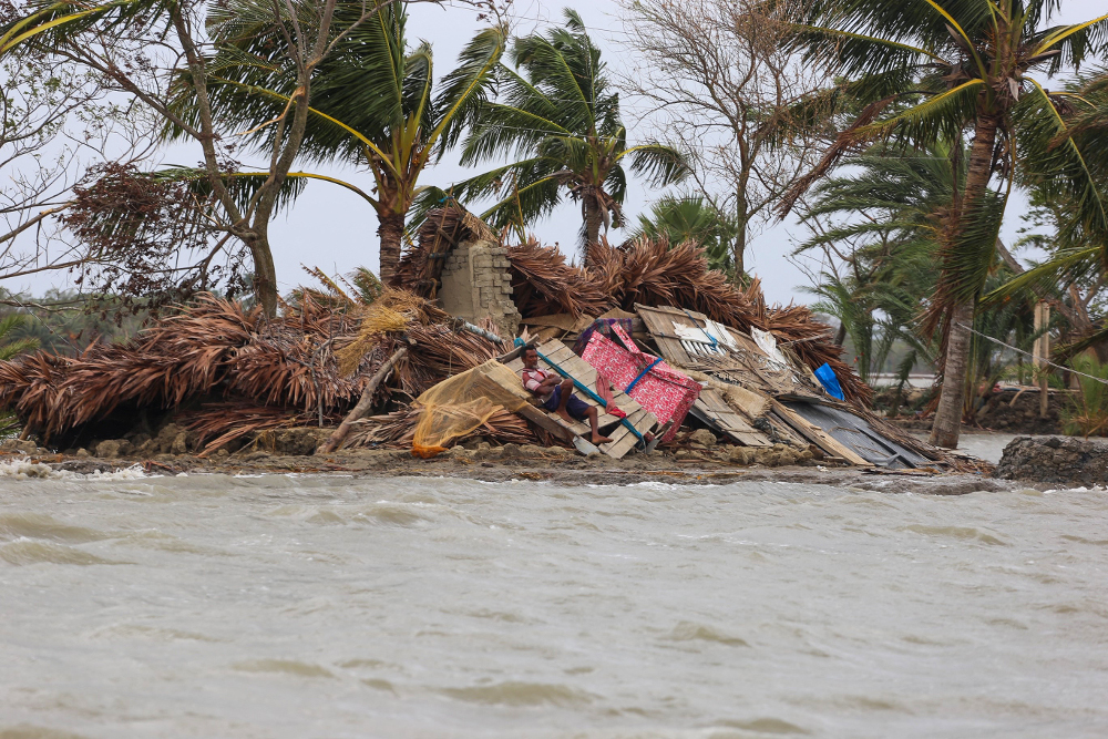 A man rests on the debris of his home surrounded by floodwater a week after Cyclone Amphan ravaged the area in Koyra, Satkhira, in Bangladesh, May 27, 2020.