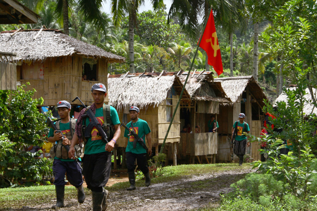 Members of the New People's Army, armed wing of the Communist Party of the Philippines, walk past a hammer-and-sickle flag displayed in a village on the southern island of Mindanao, Dec.26, 2014. [AFP]