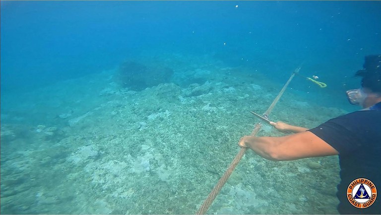 In this image released Sept. 25, 2023, a member of the Philippine coast guard cuts a rope attached to a floating barrier installed by China that blocked the entrance to Scarborough Shoal. (Philippine Coast Guard via AFP)