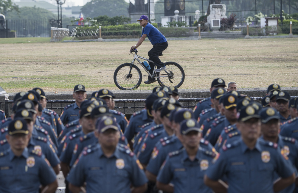 A man rides his bicycle past police standing in formation during an inspection at the police district of Manila, March 16, 2018. (Photo: AFP)