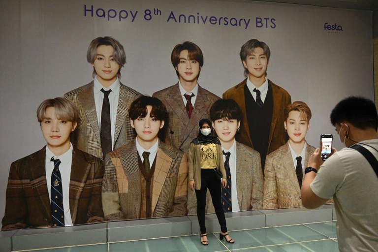 Seorang penggemar K-pop BTS berpose dengan poster raksasa anggota band tersebut di sebuah pusat perbelanjaan di Jakarta pada 21 Juni 2021. [Goh Chai Hin/AFP]