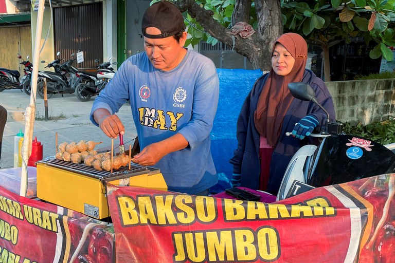 Rahmat Hidayat, 44, melayani pelanggan sambil menyiapkan jualan bakso bakarnya di Karawang, Jawa Barat, 31 Juli 2024. Ia terkena PHK saat pabrik sepatu tempatnya bekerja tutup tahun lalu. [Stefanno Sulaiman/Reuters]
