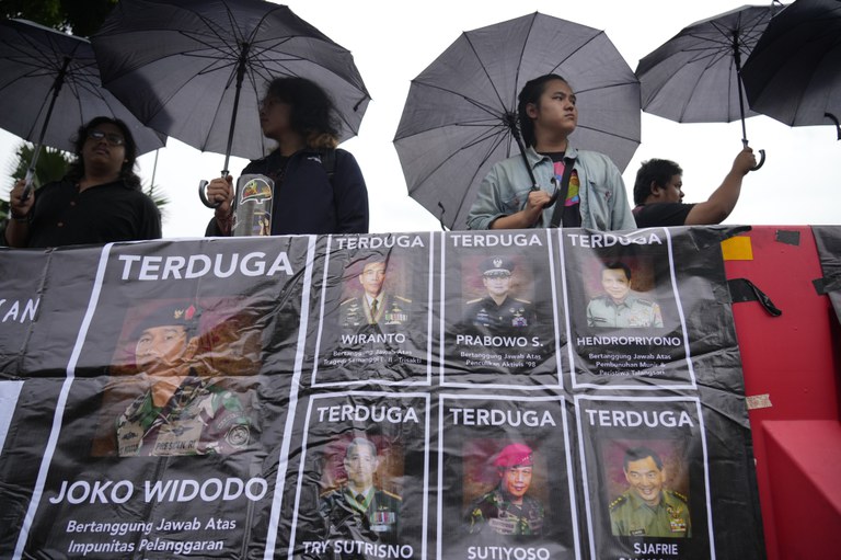 Para aktivis memegang payung sambil memajang spanduk bergambar para jenderal Angkatan Darat yang mereka tuduh melakukan pelanggaran hak asasi manusia di masa lalu, termasuk Menteri Pertahanan dan presiden terpilih Prabowo Subianto (tengah atas) dalam “Aksi Kamisan", protes mingguan yang diadakan oleh keluarga korban pelanggaran hak asasi manusia di Indonesia, di luar Istana Merdeka di Jakarta, Kamis, 29 Februari 2024. [Achmad Ibrahim/AP]