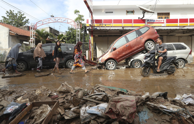 Warga berjalan di dekat kendaraan yang terbawa banjir di Bekasi, Jawa Barat, 3 Januari 2020. AP   