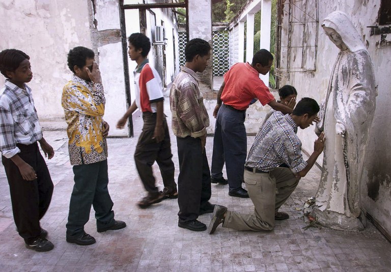 Dalam foto pada 17 Oktober 1999 ini, umat memberikan penghormatan kepada patung Bunda Maria yang rusak di rumah pemenang Hadiah Nobel Perdamaian, Uskup Carlos Belo, yang dibakar hingga hancur oleh milisi pro-Indonesia yang tidak puas dengan hasil referendum yang disponsori PBB di Dili, Timor Timur. [Charles Dharapak/AP]