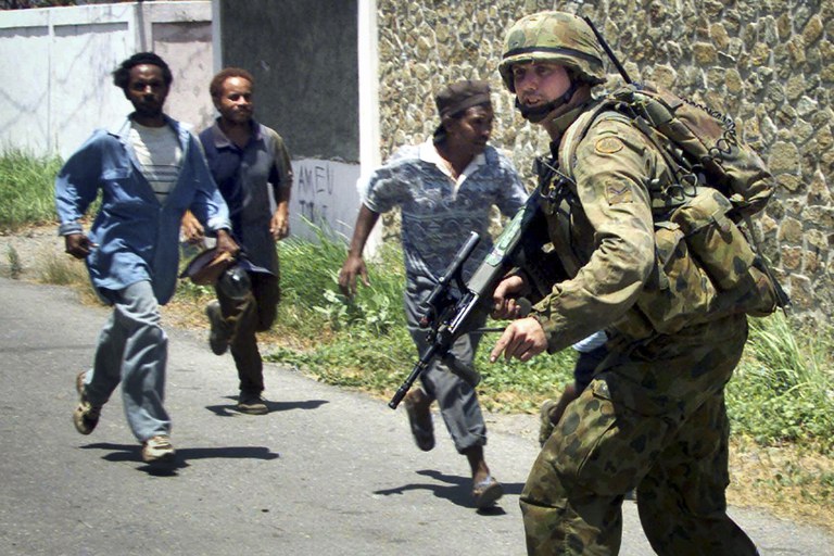 Tentara penjaga perdamaian Australia bersiap mengambil posisi saat warga berlari mencari perlindungan setelah terjadi tembakan di Dili, Timor Timur, 23 September 1999. [Charles Dharapak/AP]