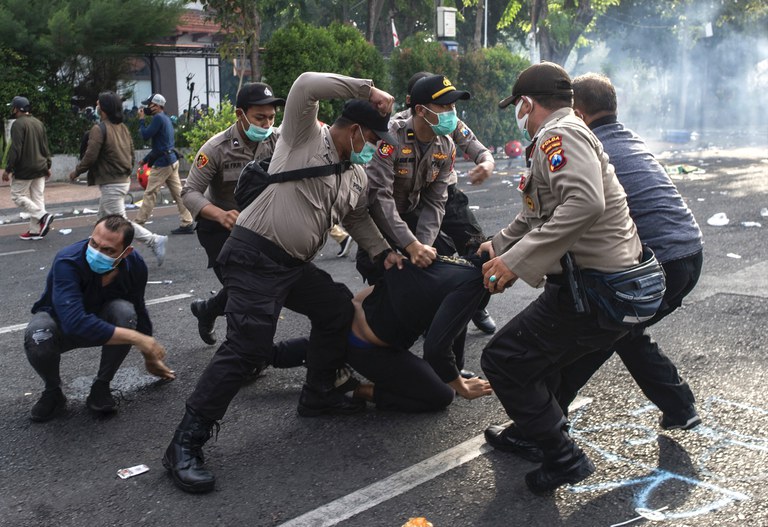 Sejumlah polisi menangkap seorang pengunjuk rasa di tengah demonstrasi di Surabaya yang menentang Undang-Undang Cipta Karya atau dikenal dengan sebutan Omnibus Law yang dinilai sejumlah pengamat dan aktivis hak asasi manusia dibuat untuk mempermudah para investor berinvestasi dengan mengorbankan hak buruh dan lingkungan hidup, pada 8 Oktober 2020. [Juni Kriswanto/AFP]