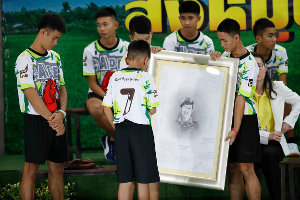 นายเอกพล จันทะวงษ์ หรือโค้ชเอก (ซ้าย) และสมาชิกทีมหมูป่าอ่านคำไว้อาลัยบนภาพ จ่าแซม หรือ นาวาตรี สมาน กุนัน อดีตหน่วยซีล ที่อาสาเข้าร่วมภารกิจกู้ภัยและเสียชีวิตในถ้ำหลวง ก่อนที่จะช่วยเด็กทีมหมูป่าออกมาได้ ระหว่างแถลงข่าวในจังหวัดเชียงราย 18 กรกฎาคม 2561 (เอพี)